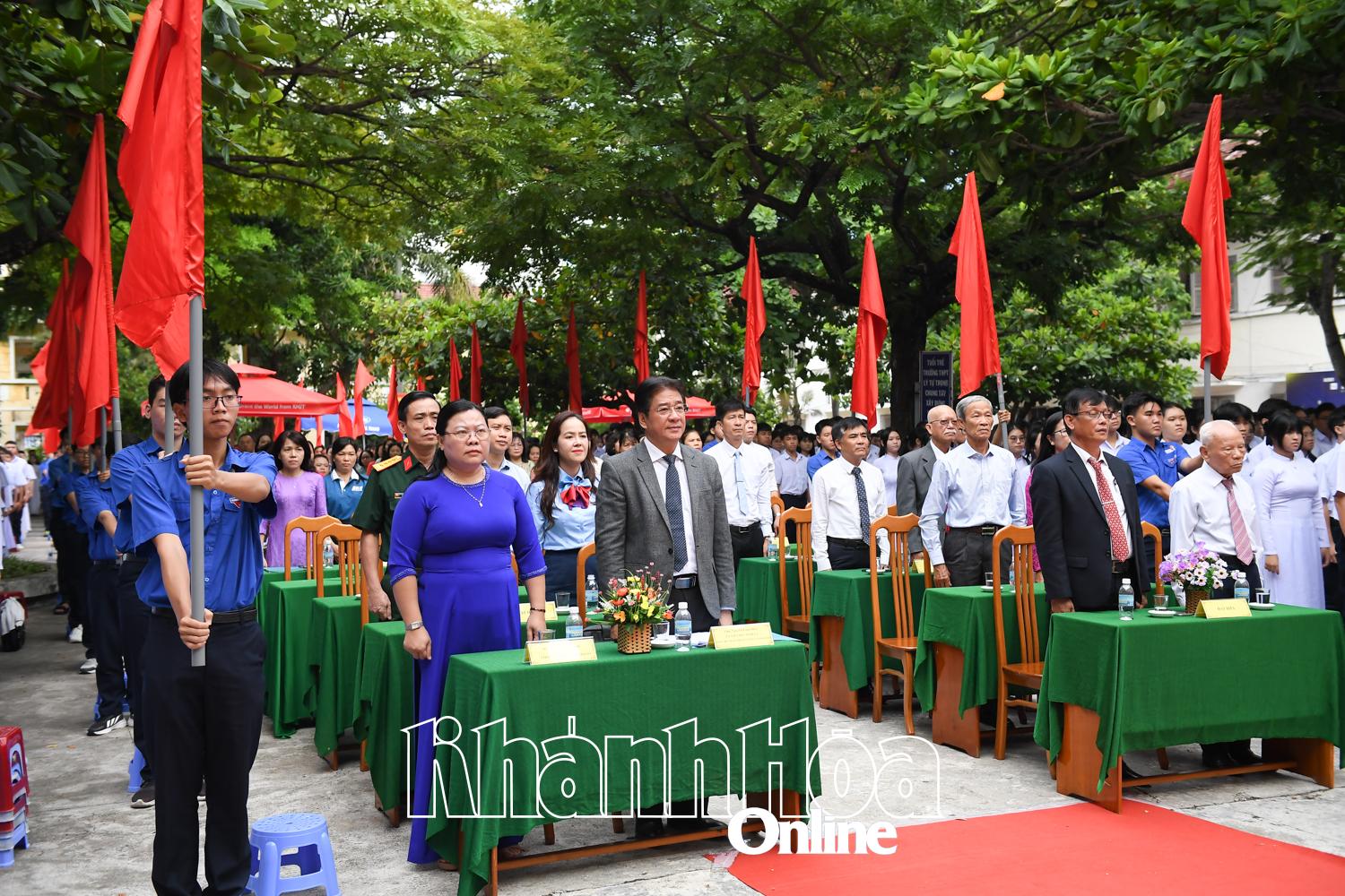 Các đại biểu, giáo viên và học sinh thực hiện nghi thức chào cờ, hát Quốc ca.